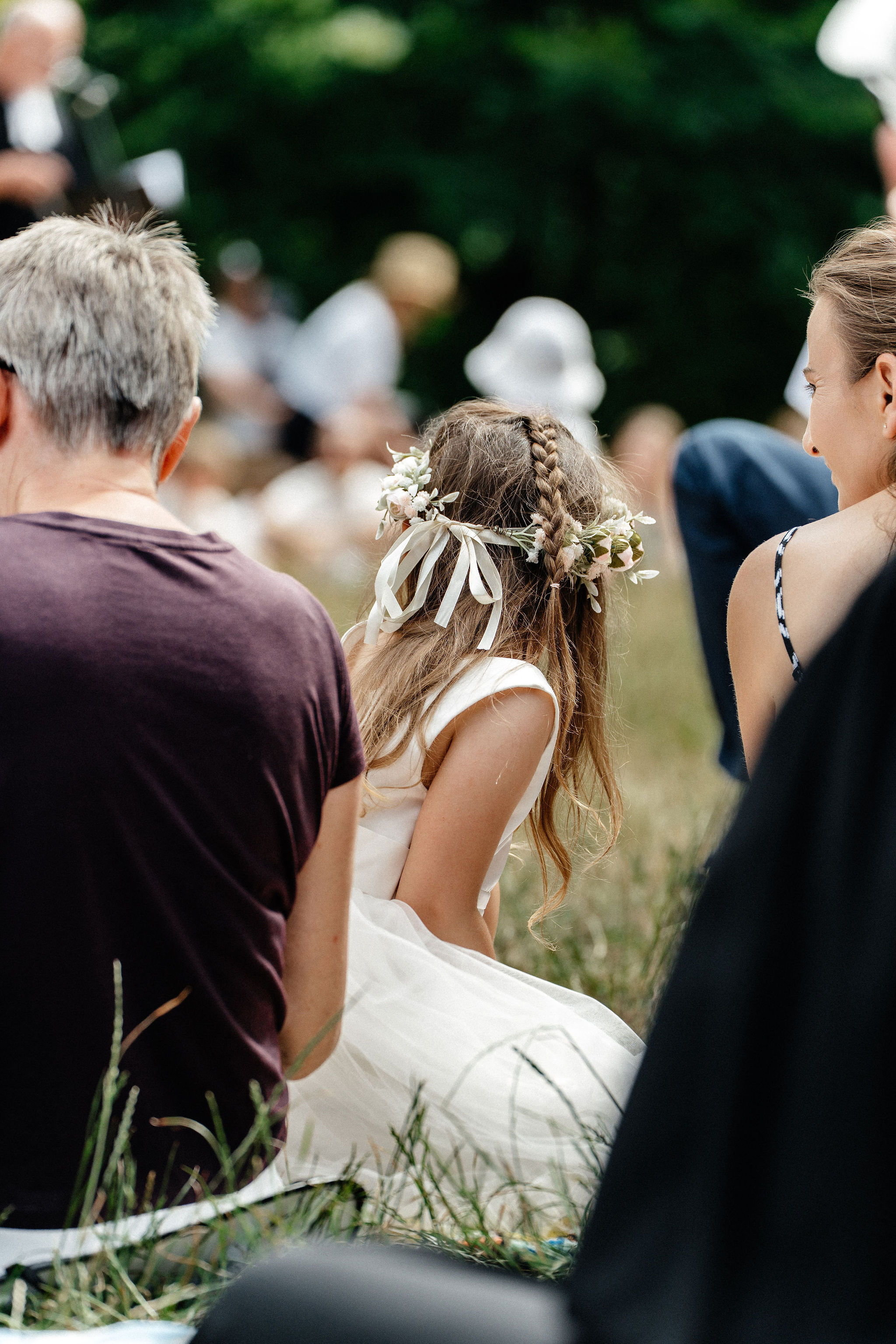 Mädchen mit Blumenschmuck im langen Haar und weißem Kleid von hinten in der Gemeinde (Ausschnitt)