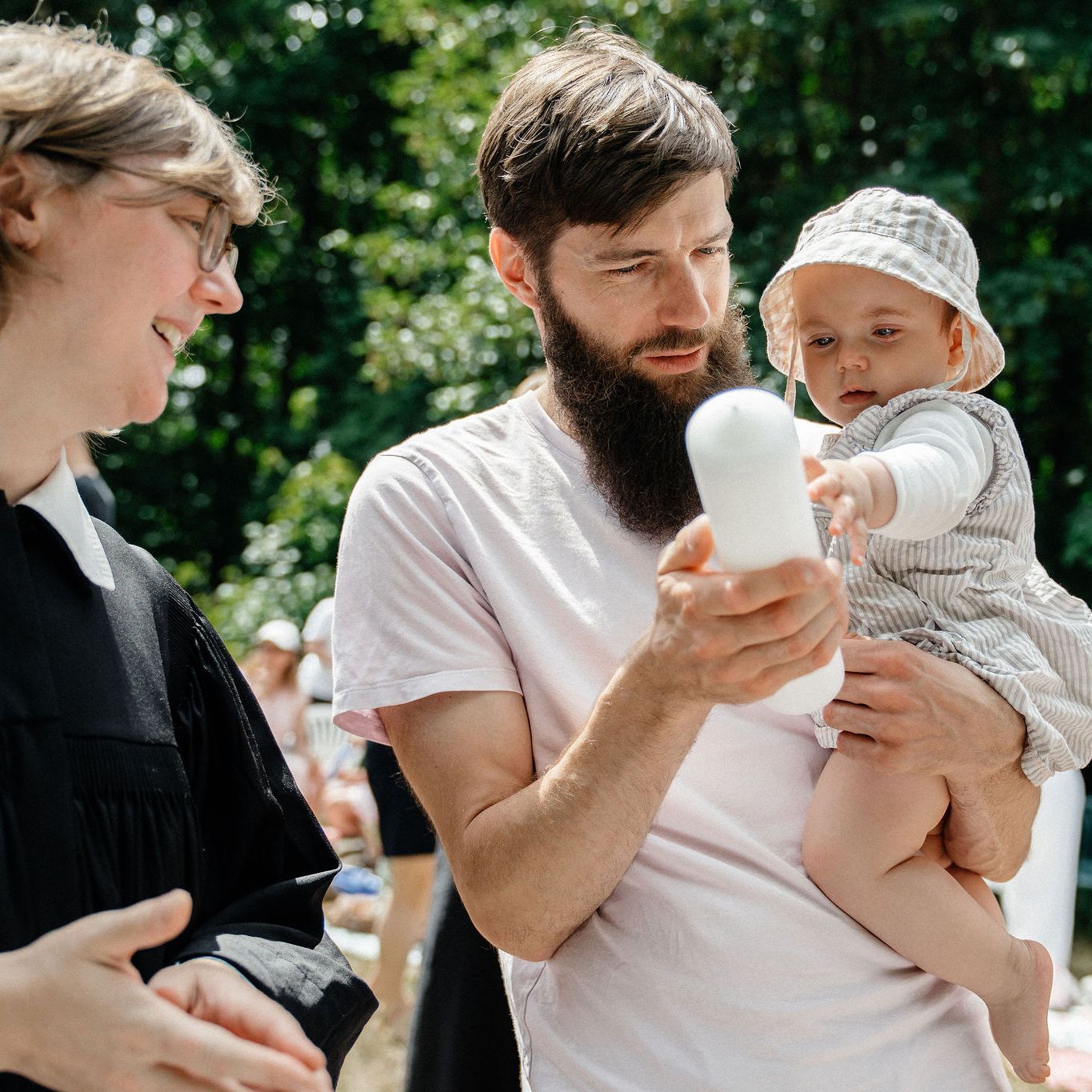 Pfarrerin, Vater mit Kind auf dem Arm, das auf die Taufkerze zeigt
