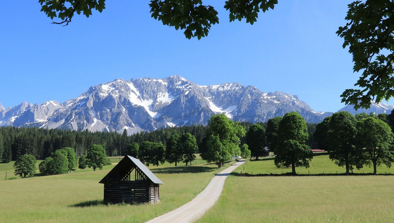 Hohe Berge mit Schnee und ein Weg mit Heuschober am Wegesrand in der Region Ramsau 